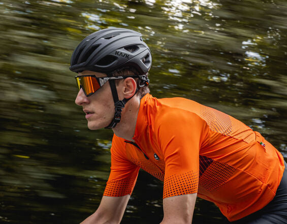 Wielrenner in oranje fietsshirt in beweging, zijaanzicht met bewegingsonscherpte