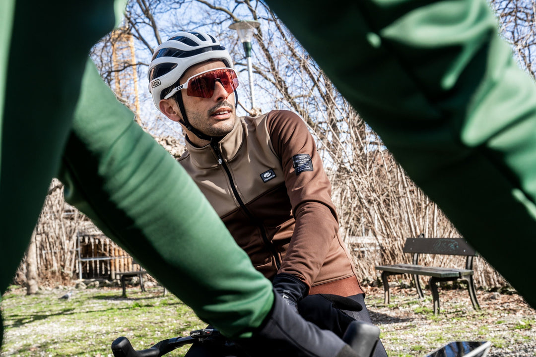 Renner in bruine fietsjas met groene mouwen op de fiets in het voorjaar