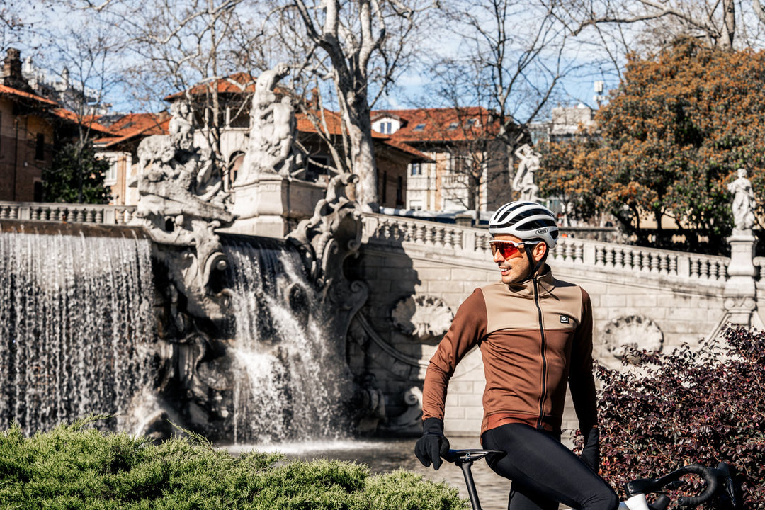 Parentini Unica Dark Clay — winterfietsjas gedragen naast de fiets bij een fontein