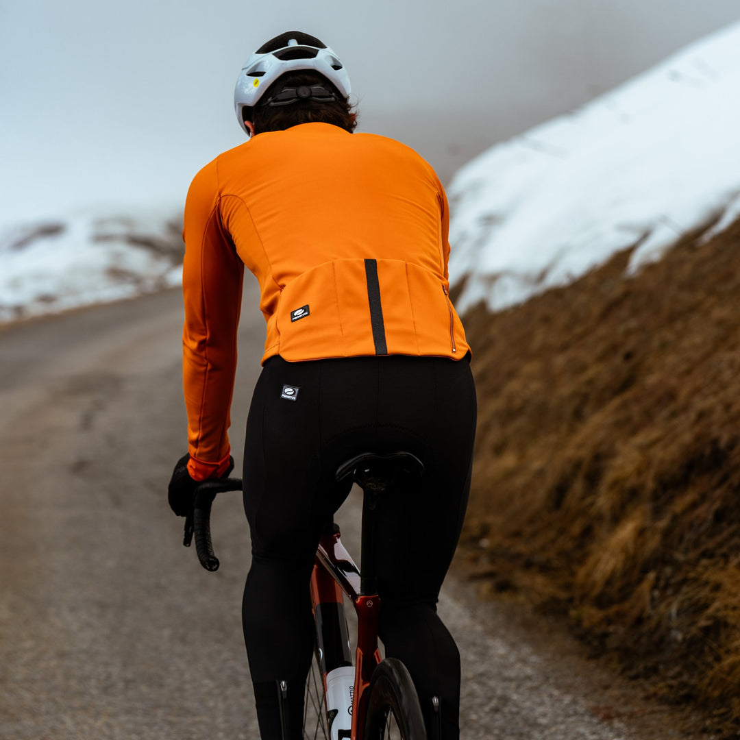 Wielrenner in oranje Parentini winterjack en zwarte INGA Intenso K-Dry bibtight op een besneeuwde bergweg
