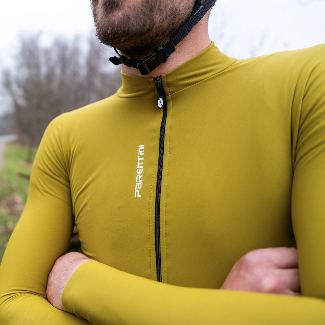 Parentini Unica longsleeve reed grass — gedragen met gekruiste armen, close-up van rits en verticaal Parentini-logo