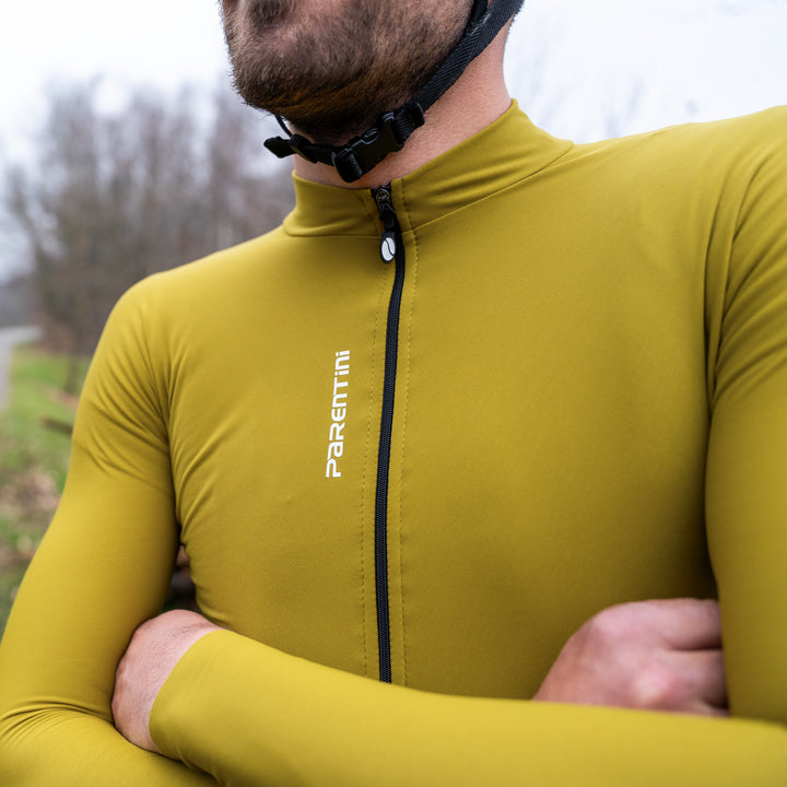 Parentini Unica longsleeve reed grass — gedragen met gekruiste armen, close-up van rits en verticaal Parentini-logo